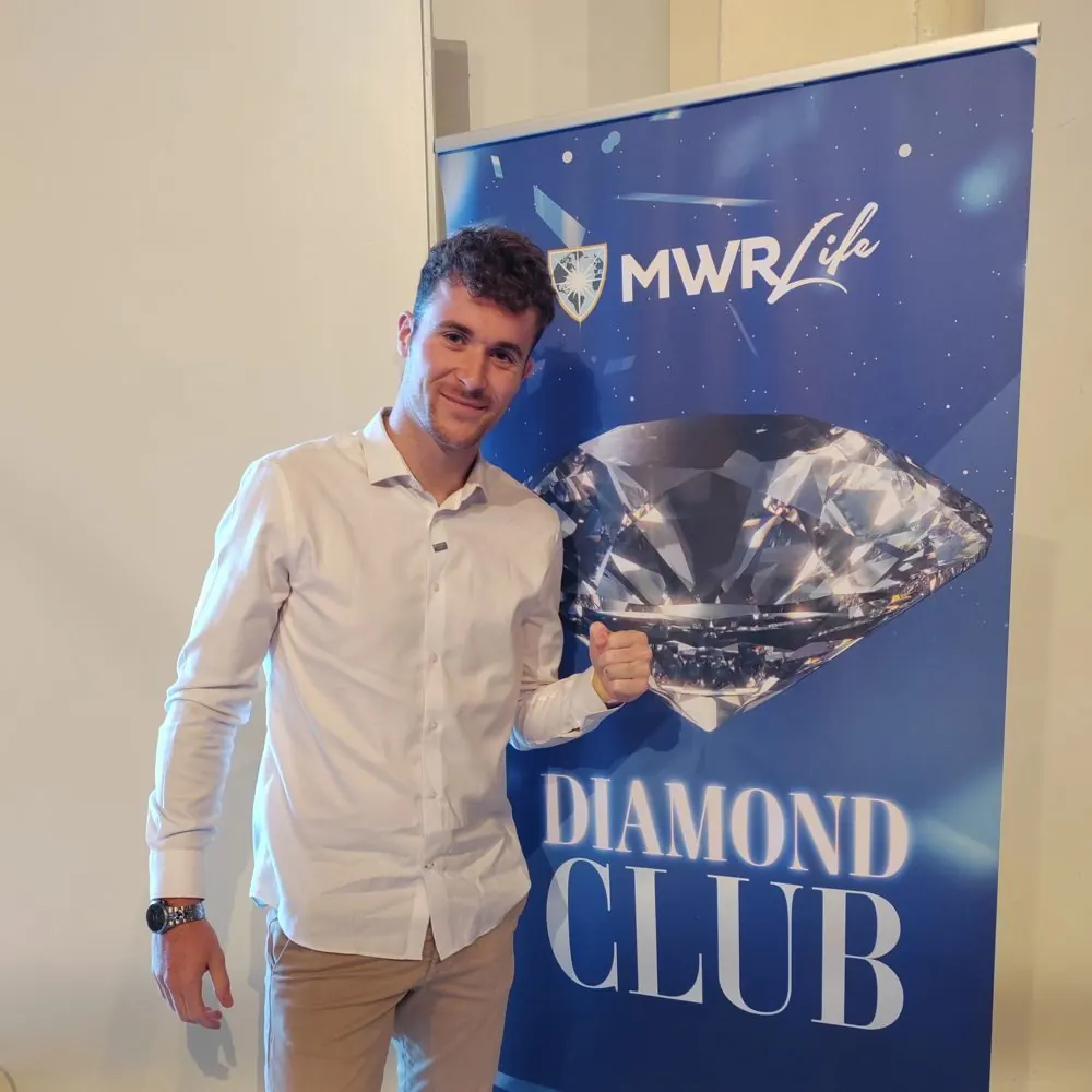 Julien en chemise blanche devant le kakémono Diamond Club de MWR Life